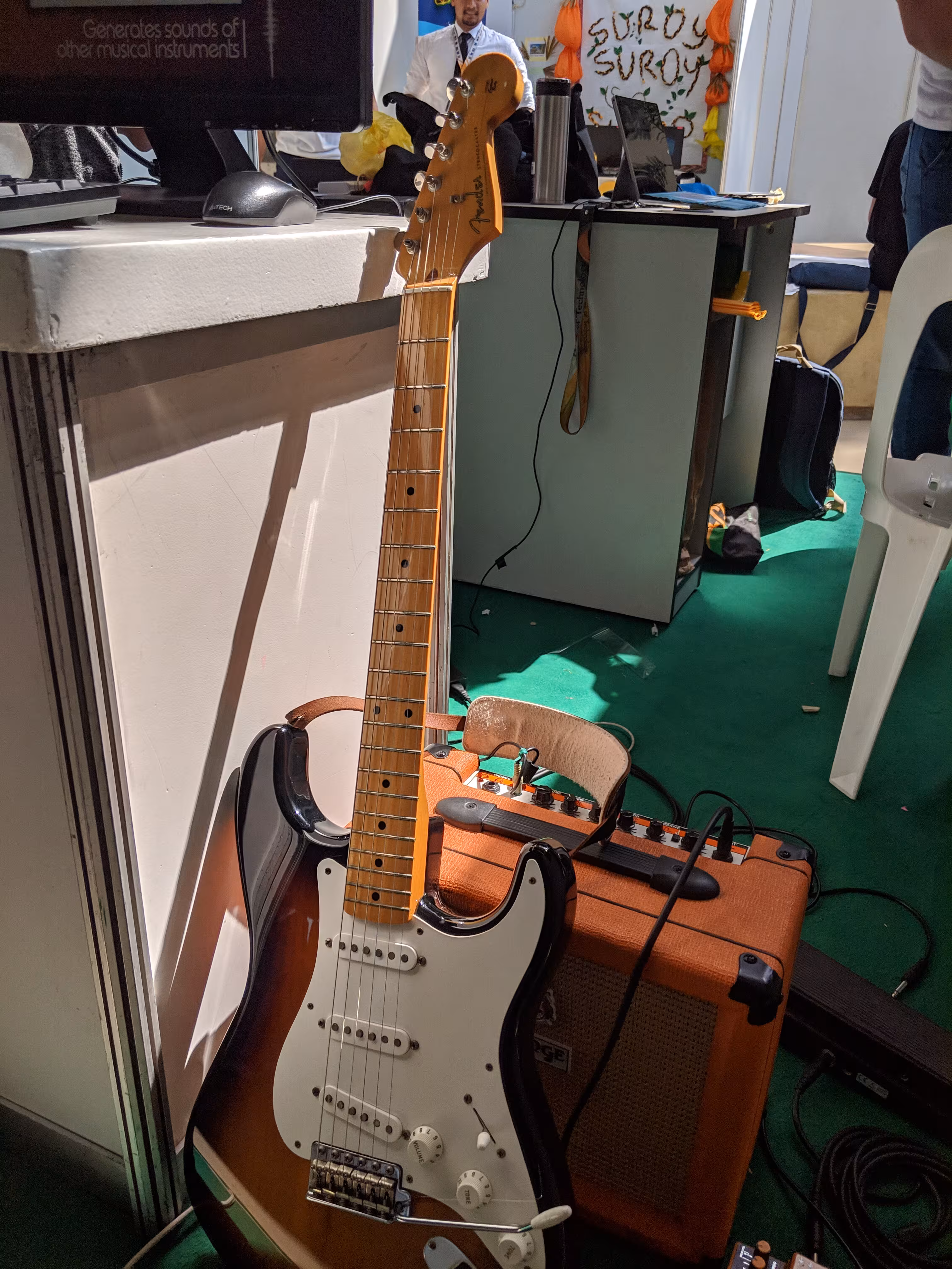 A Fender Stratocaster leaning against a table next to it and an Orange amplifier behind it