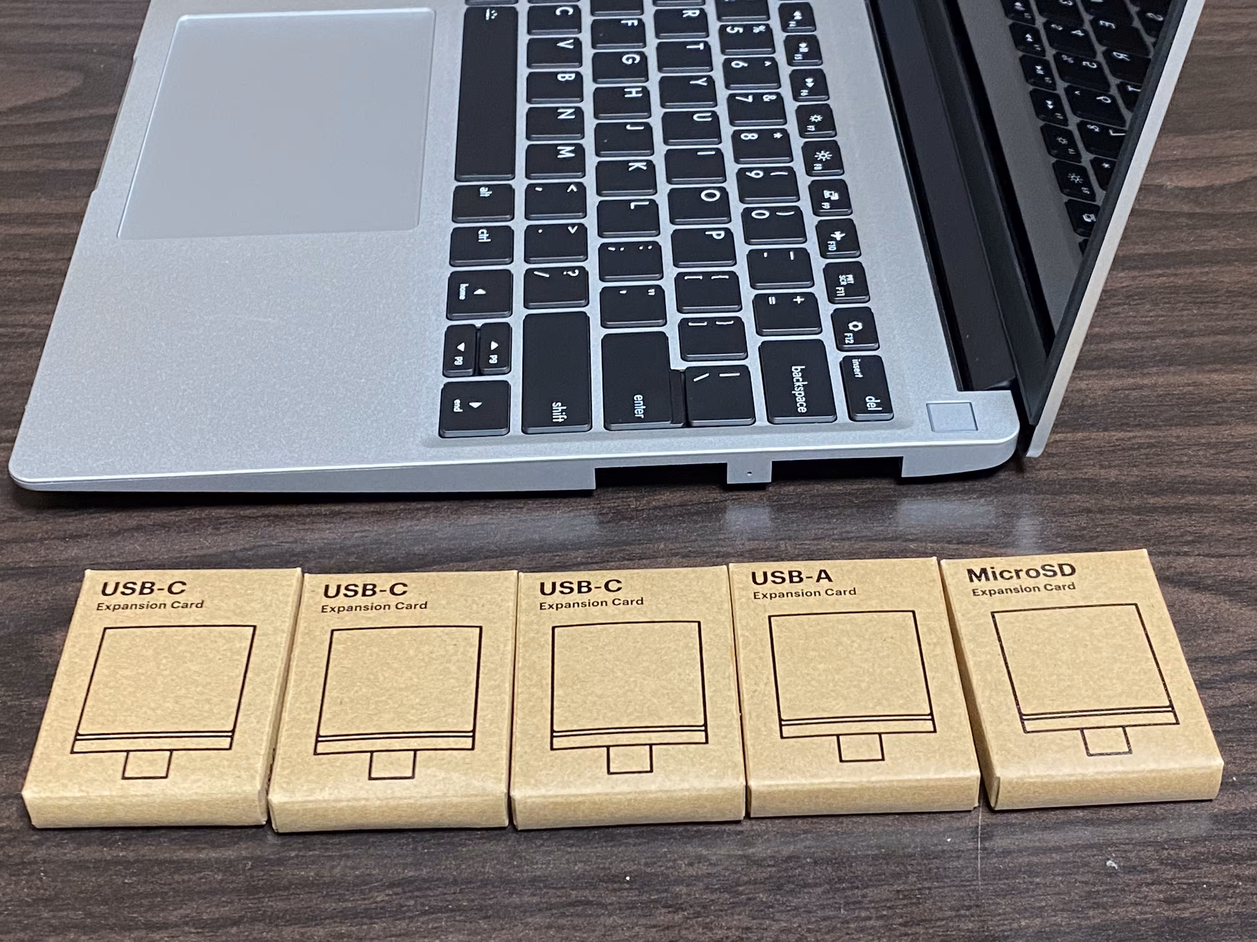 A Framework Laptop 13 next to five unopened boxes of expansion cards. The expansion cards, from left to right, are USB-C, USB-C, USB-C, USB-A, and MicroSD cards.